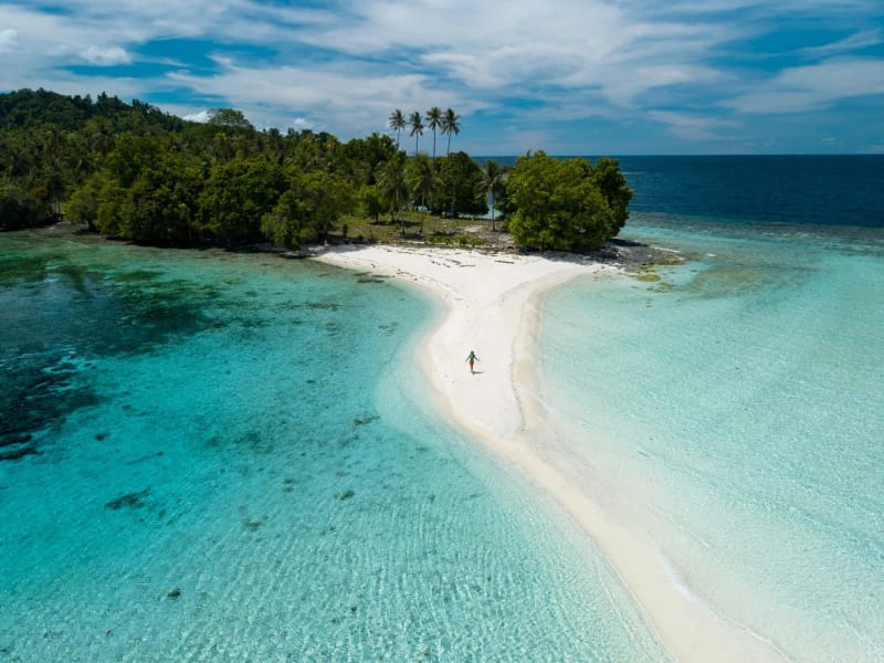 A white sandbar running from a forested island into shallow turquoise water on a sunny day